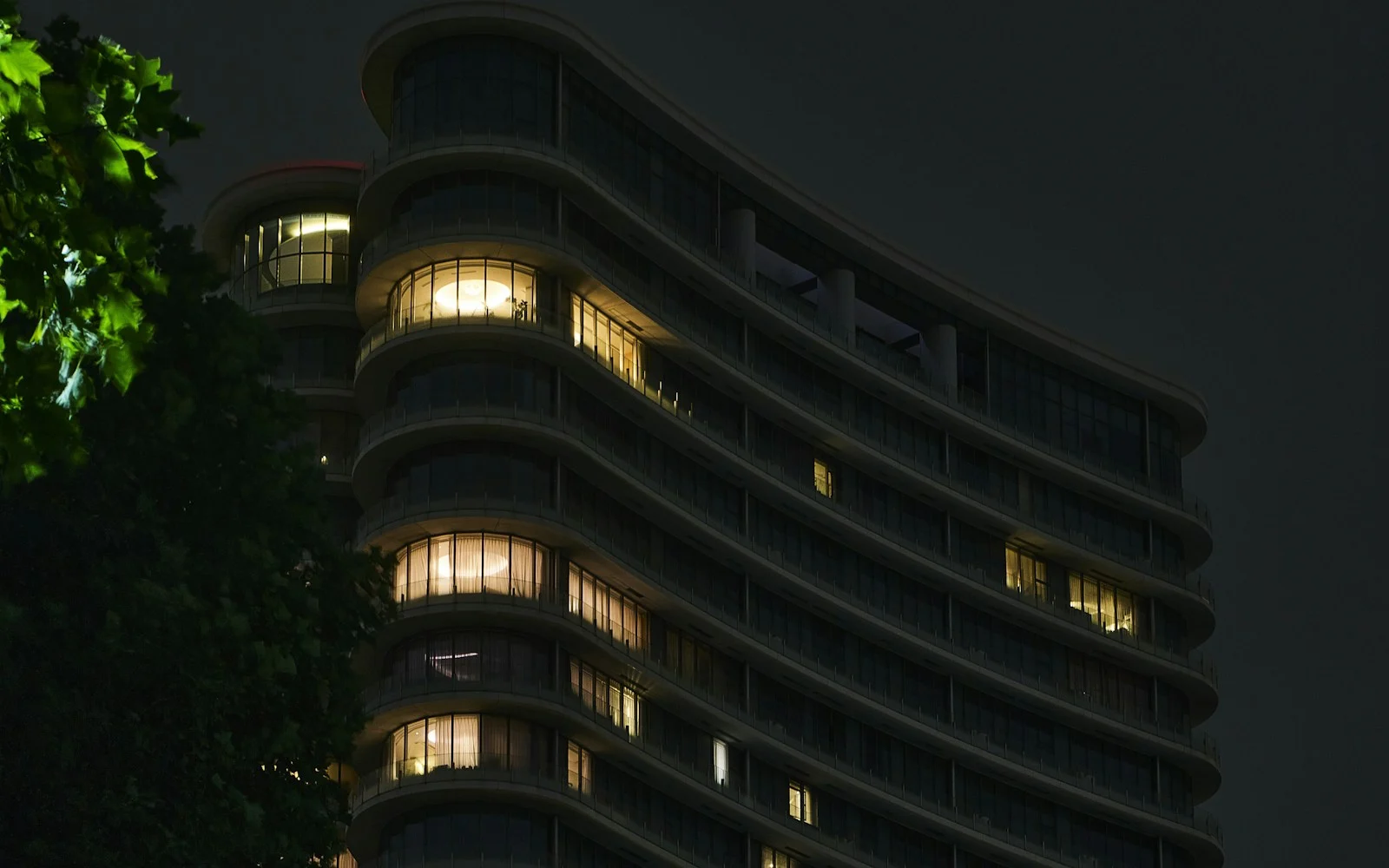 A curved office building at night with rows of glowing windows