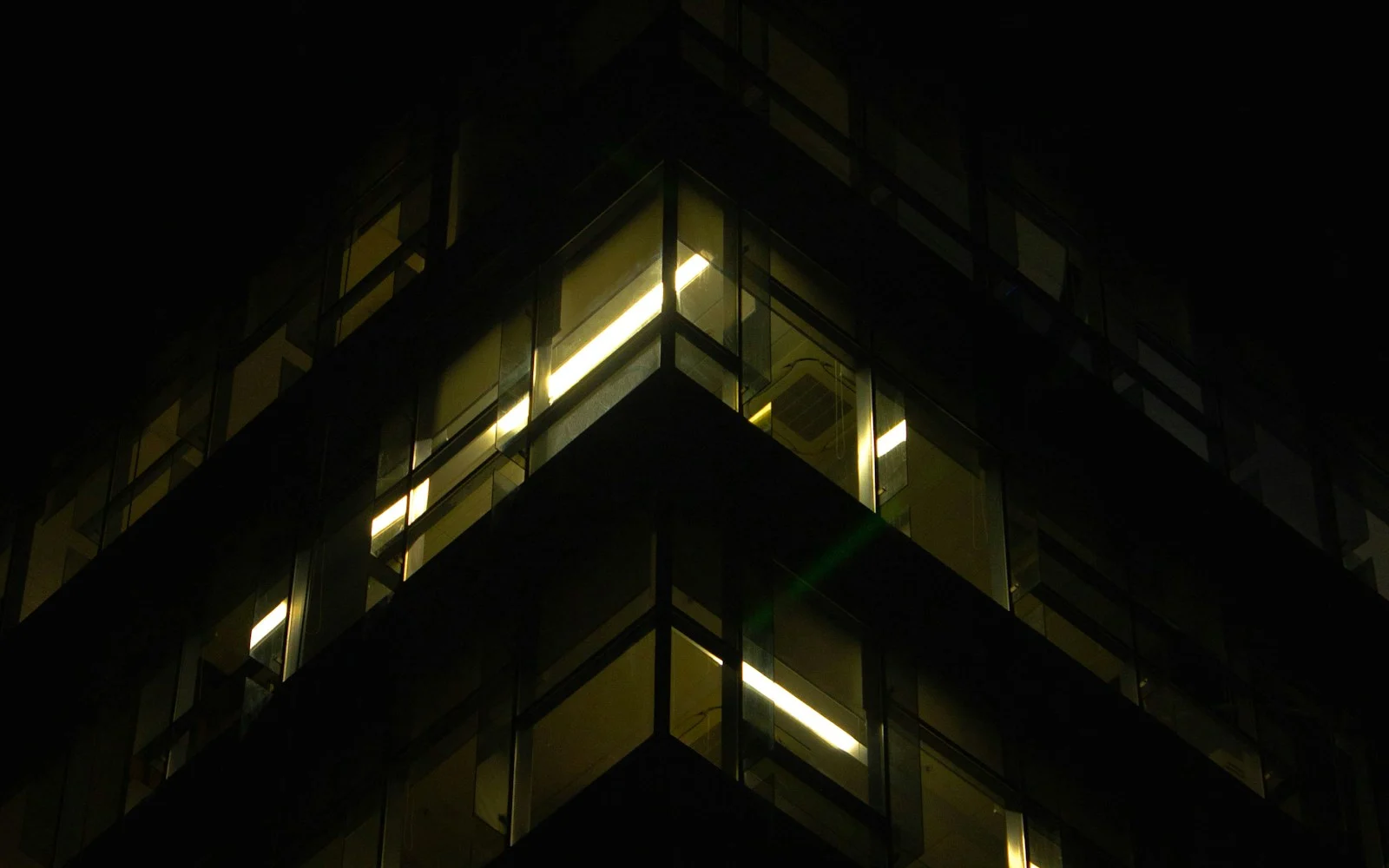 A dark tower at night, a few office windows still lit
